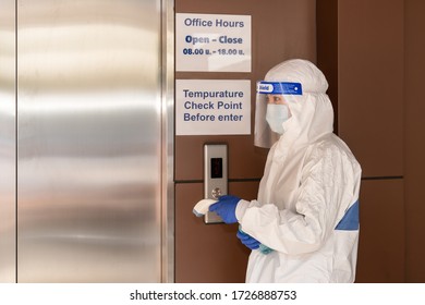 Heath Officer In Coronavirus Covid-19 Protection Coverall Clothing With Digital Temperature Scanning Device On Hand Standing In Front Of Office Building Elevator Check Point