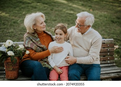 Heathy senior couple sitting on the bench witht heir cute little granddaughter - Shutterstock ID 2074920355