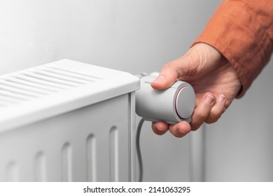 heating, energy crisis and consumption concept - close up of hand turning radiator toggle switch at home