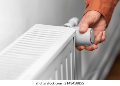 heating, energy crisis and consumption concept - close up of hand turning radiator toggle switch at home - Shutterstock ID 2143458855
