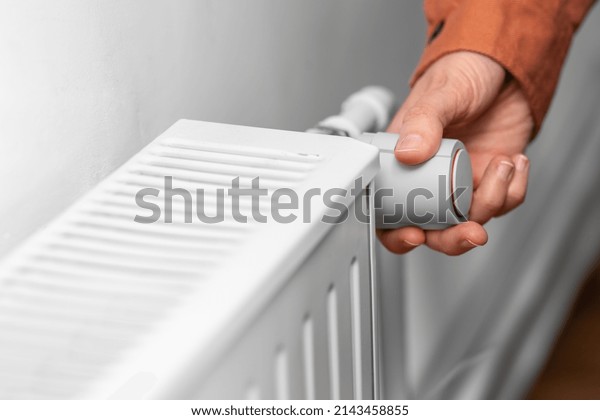 heating, energy crisis and\
consumption concept - close up of hand turning radiator toggle\
switch at home