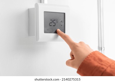 heating, energy and power consumption concept - close up of hand setting room temperature on thermostat at home