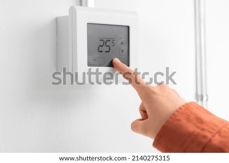 heating, energy and power consumption concept - close up of hand setting room temperature on thermostat at home