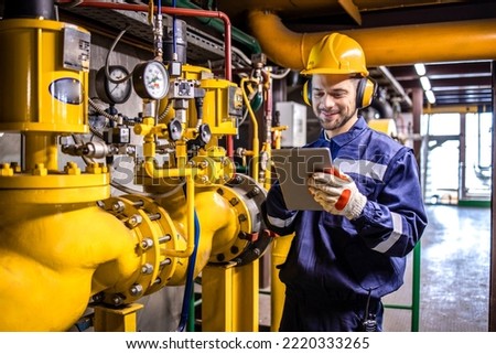 Heating plant technician standing by gas pipes and maintaining temperature inside power plant boiler room.