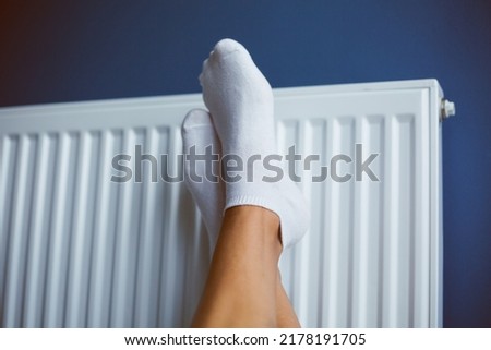Heating radiator. A woman warms her feets at the battery. heating season. Energy. High quality photo