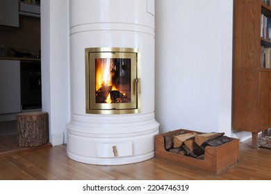 Heating With Wood: White Round Wood Burning Stove In Living Room, Firewood In Box And Tree Stump For Sitting. 