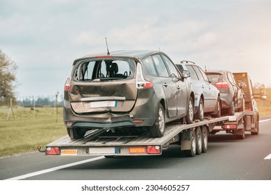 A heavily damaged cars on a trailer is being towed by a tow truck. - Shutterstock ID 2304605257