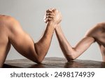 Heavily muscled man arm wrestling a puny weak man. Arms wrestling thin hand, big strong arm in studio. Two man