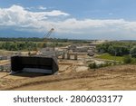 Heavy Construction Equipment Assembling Precast Concrete Viaduct Over Stream For Major Highway Expansion Under Dramatic Summer Sky