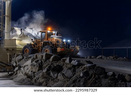 Heavy construction and mining machinery unloading gravel into silos on the night shift. Close-up.
