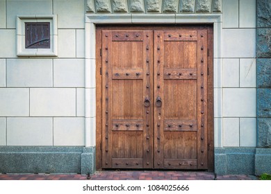 Heavy doors made of wooden boards with round handles against the gray wall