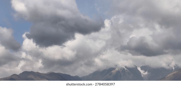 Heavy dramatic storm clouds gathering over distant snow-capped mountain peaks on a moody overcast day
