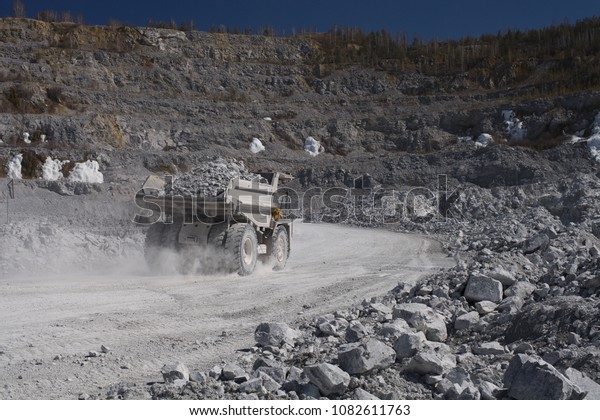 Heavy dump-body truck loaded with limestone\
ore moves along the road in a quarry, back view. Mining industry.\
Heavy equipment.