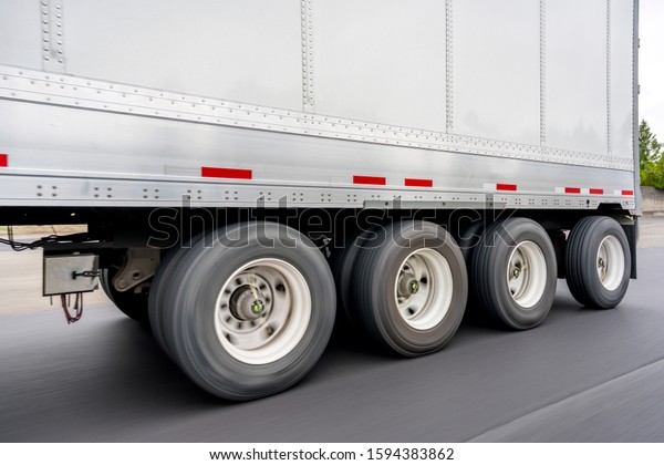 Heavy - duty big rig semi truck transporting dry van\
four-axle semi trailer for transportation over heavy loads with\
weight distribution along the axles running on the highway\
road