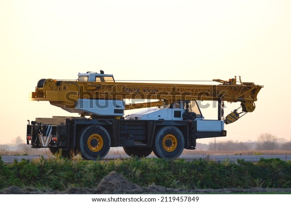 Heavy duty mobile lifting crane driving on\
intercity road at sunset