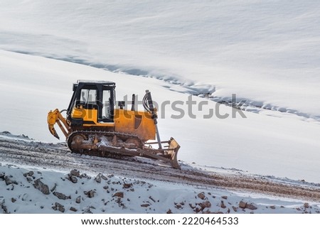 Heavy duty road building machinery bulldozer or earthmover on construction site on snowcovered hill in winter