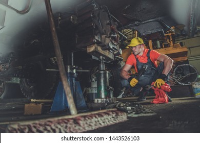 Heavy Equipment Repair Shop. Caucasian Professional Mechanic Fixing Excavator Undercarriage. Industrial Theme.