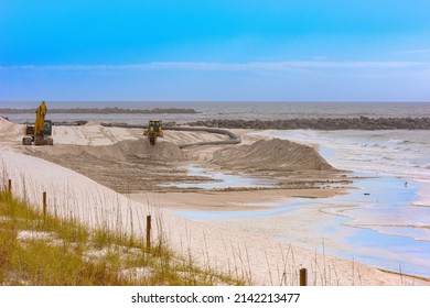 Heavy equipment replenish shoreline with sand as it's dredged from the pass