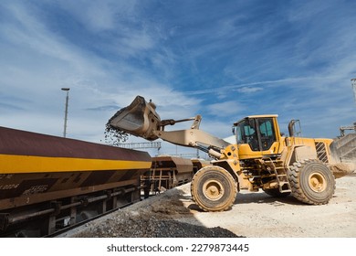 heavy excavator is loading stone agregate on railroad wagons
