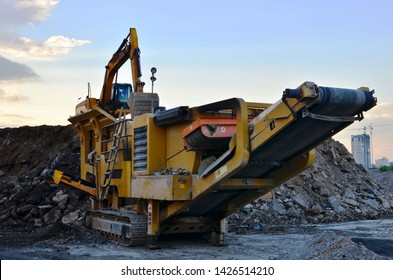 Heavy excavator working at construction site. Unloading old stone or concrete waste into a mobile cheek crusher for crushing and processing them into gravel or cement. 