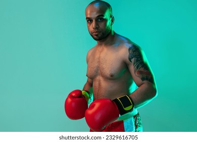 Heavy fists. Close-up portrait of young male boxer in red gloves standing on blue green neon background. Healthy lifestyle, sport, motion concept. Copy space for ad. - Powered by Shutterstock