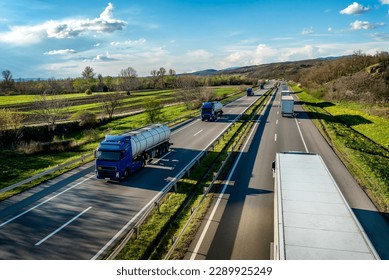 Heavy Highway transportation scene with Convoy of white transportation trucks in one way and blue tank tracks passing in the opposite way on rural highway under a beautiful blue sky