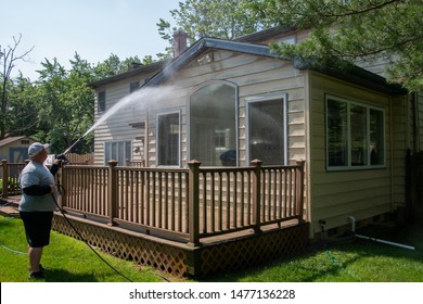 Heavy Husband Power Washing The Siding On The Back Of A House Over A Brown Wooden Deck