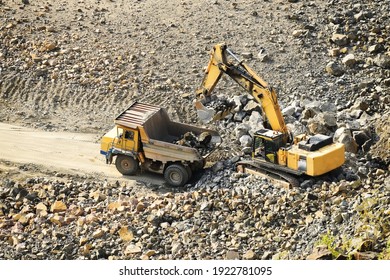 heavy industrial machinery works in a rock loading quarry. A crane loads granite stones in a quarry onto a truck. View from above.