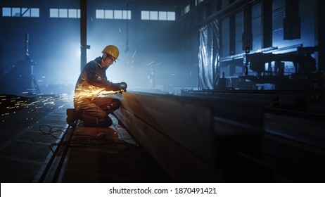 Heavy Industry Engineering Factory Interior with Industrial Worker Using Angle Grinder and Cutting a Metal Tube. Contractor in Safety Uniform and Hard Hat Manufacturing Metal Structures. - Powered by Shutterstock