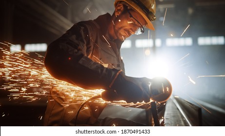 Heavy Industry Engineering Factory Interior with Industrial Worker Using Angle Grinder and Cutting a Metal Tube. Contractor in Safety Uniform and Hard Hat Manufacturing Metal Structures. - Shutterstock ID 1870491433