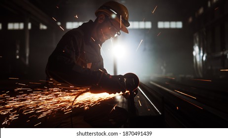 Heavy Industry Engineering Factory Interior with Industrial Worker Using Angle Grinder and Cutting a Metal Tube. Contractor in Safety Uniform and Hard Hat Manufacturing Metal Structures. - Shutterstock ID 1870491439