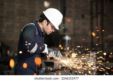 Heavy Industry Engineering Factory Interior with Industrial Worker Using Angle Grinder and Cutting a Metal Tube. Contractor in Safety Uniform and Hard Hat Manufacturing Metal Structures. - Powered by Shutterstock