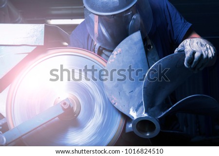 Heavy industry manual worker with big grinder and boat propeller