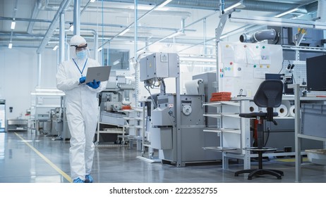 Heavy Industry Manufacturing Factory: Scientist in Sterile Coverall Walking with Laptop Computer, Examining Industrial CNC Machine Settings and Configuring Production Functionality. - Shutterstock ID 2222352755