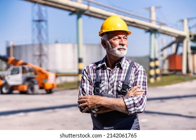 Heavy industry, power plant, oil refinery, and factory staff. An experienced senior factory worker with a helmet on his head standing in a refinery yard with arms crossed and looking away. - Shutterstock ID 2142061765
