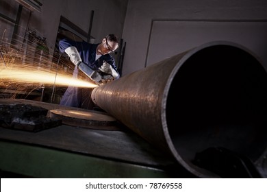 Heavy industry worker cutting steel pipe with angle grinder in workshop.