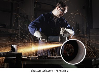 Heavy industry worker cutting steel pipe with angle grinder in workshop.