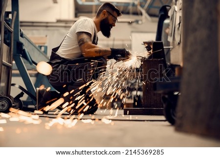 A heavy industry worker kneeling and using grinder at workshop.