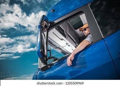 Heavy Load Cargo Delivery. Caucasian Truck Driver Inside Semi Tractor Cabin And The Blue Sky. Transportation Industry.