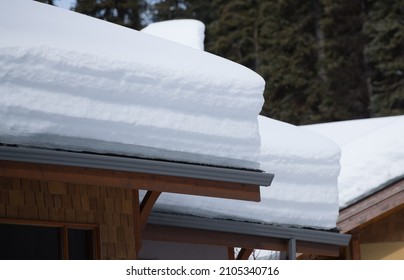heavy load of white layered snow on chalet roofs of ski resort in winter after snow fall horizontal format layers of snow above eaves trough of roof tops winter  home maintenance construction  - Powered by Shutterstock