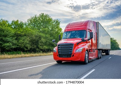 Heavy loaded classic red big rig semi truck with high roof transporting commercial cargo at dry van semi trailer running on the straight wide divided multiline highway road for timely delivery