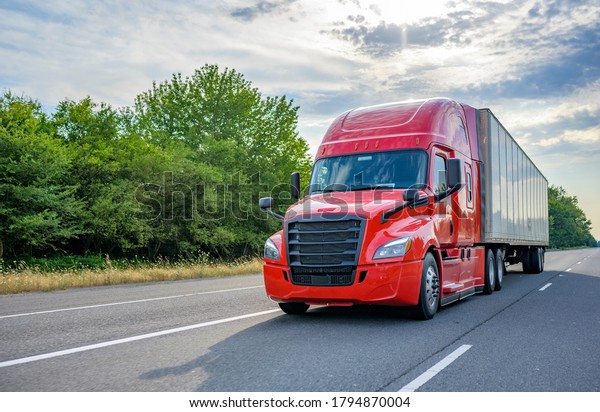 Heavy loaded classic red big rig semi truck with\
high roof transporting commercial cargo at dry van semi trailer\
running on the straight wide divided multiline highway road for\
timely delivery