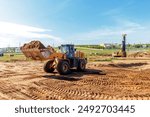 A heavy loader is moving a large amount of dirt at a construction site in an urban area on a clear day