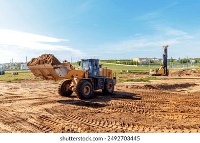 A heavy loader is moving a large amount of dirt at a construction site in an urban area on a clear day