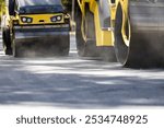 Heavy machinery compacts freshly laid asphalt as construction workers supervise the process, ensuring a smooth and durable road surface.