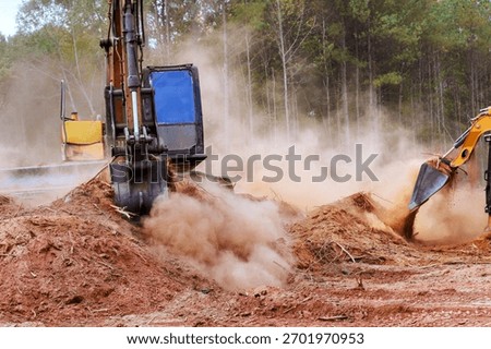 Heavy machines work to clear plot of land, creating dust clouds in forest landscape an active construction area