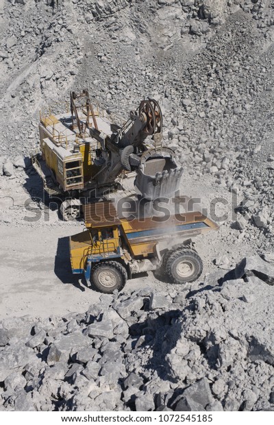 Heavy mining excavator loads rock ore into a\
heavy dump truck in a limestone quarry, close-up, top view. Heavy\
equipment. Mining\
industry.