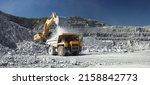 Heavy mining truck and excavator, close-up, against the background of the panorama of a limestone quarry. Long exposure of a moving excavator has a blurred image.