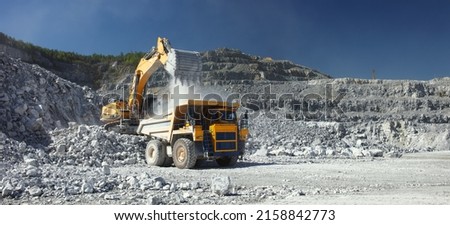 Heavy mining truck and excavator, close-up, against the background of the panorama of a limestone quarry. Long exposure of a moving excavator has a blurred image. 商業照片 © 