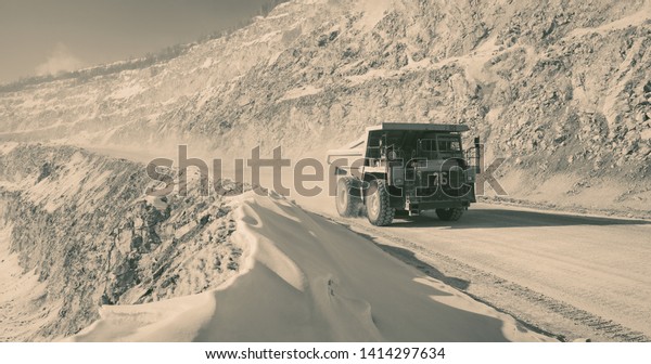 Heavy mining truck at the limestone quarry, a\
monochrome panoramic image imitating an old analog photo printing.\
Mining industry.